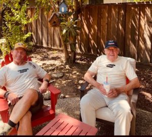 Two men, Mark R. Clifford and a fellow USMC member, sitting on red chairs in a backyard for an engaging historical fiction story set in the Marine Corps.